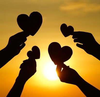 Silhouette of people's hands showing heart shaped objects while in a sunset view